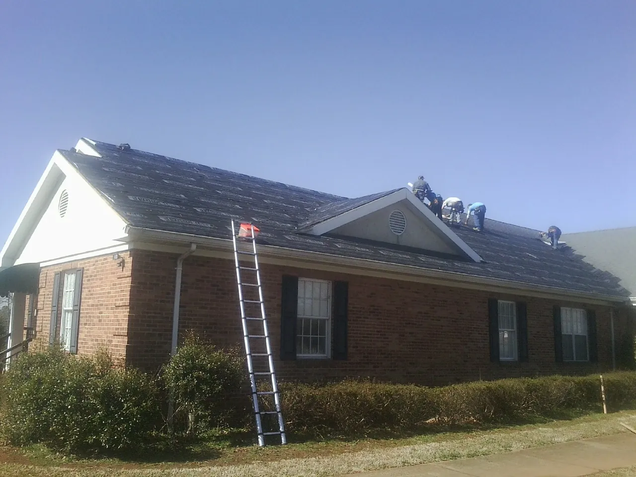 Crew tearing shingles off a brick ranch roof with a ladder set — Emergency Roof Repair work by our crew in Ferdinand